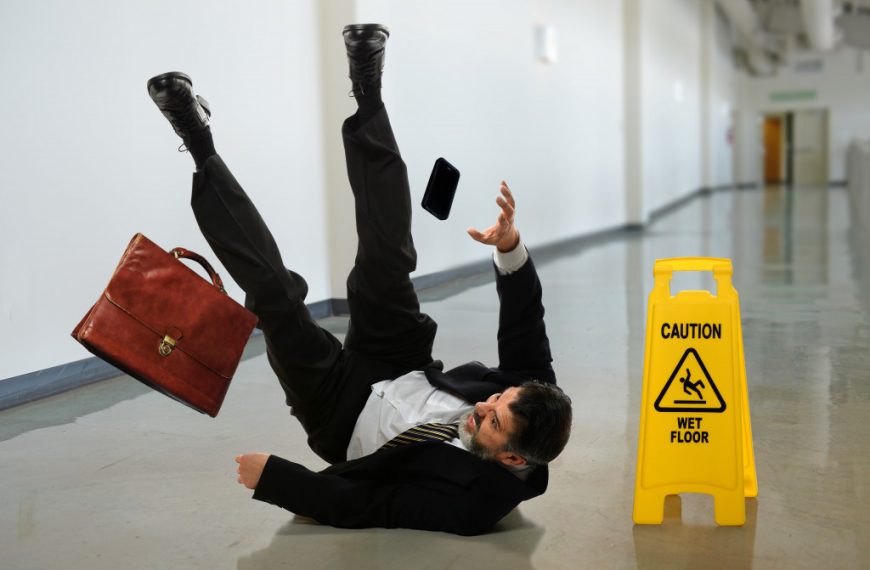 A businessman slipping and falling near a wet floor sign